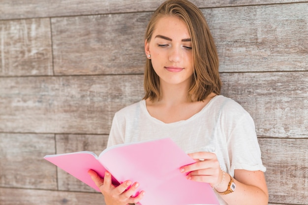 Mujer leyendo el libro inclinado sobre la pared de madera