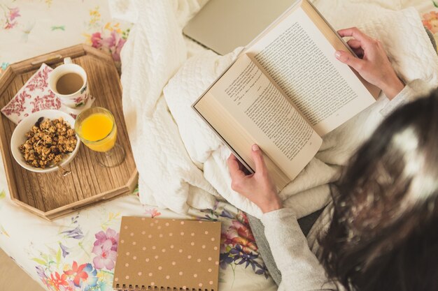 Mujer leyendo un libro mientras desayuna