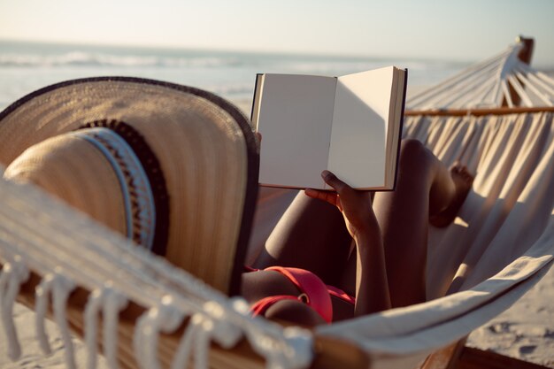 Mujer leyendo un libro mientras se relaja en una hamaca en la playa