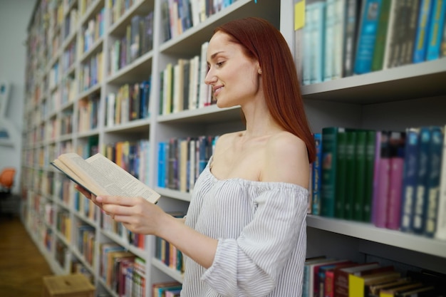 Mujer leyendo libro de pie de lado a cámara