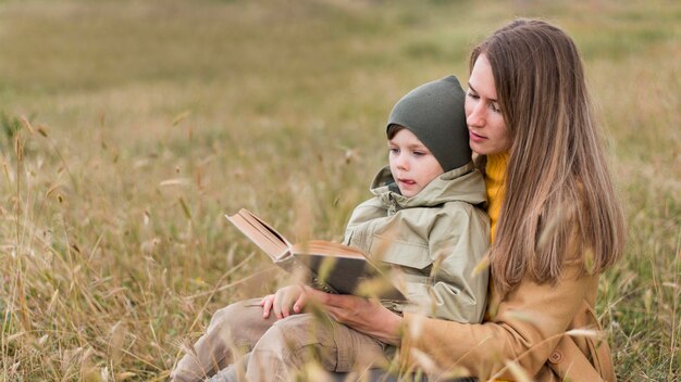 Mujer leyendo un libro a su hijo afuera