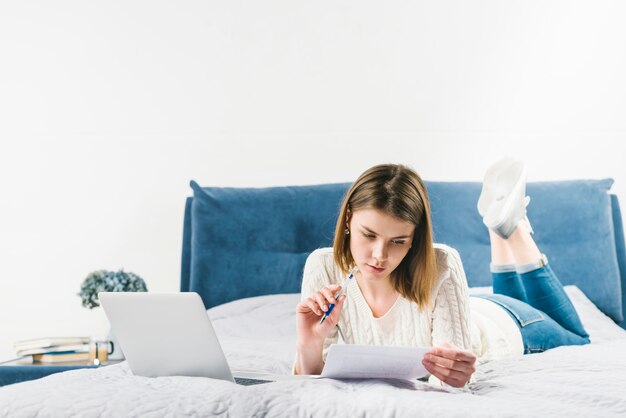 Mujer leyendo papeles cerca de la computadora portátil