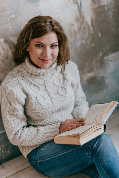 Mujer con libro cerca de la pared mirando a la cámara