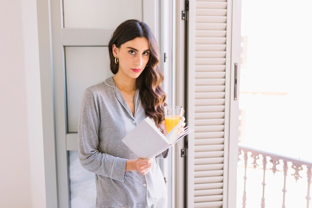 Mujer con libro y jugo junto a la ventana