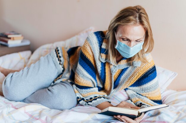 Mujer con libro y máscara médica en cuarentena en casa