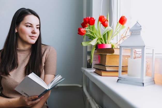 Mujer con libro sentado junto a la ventana