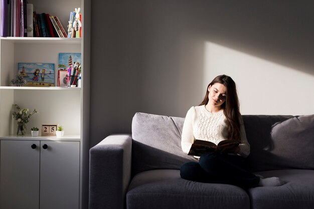 Mujer con libro en el sofá en casa