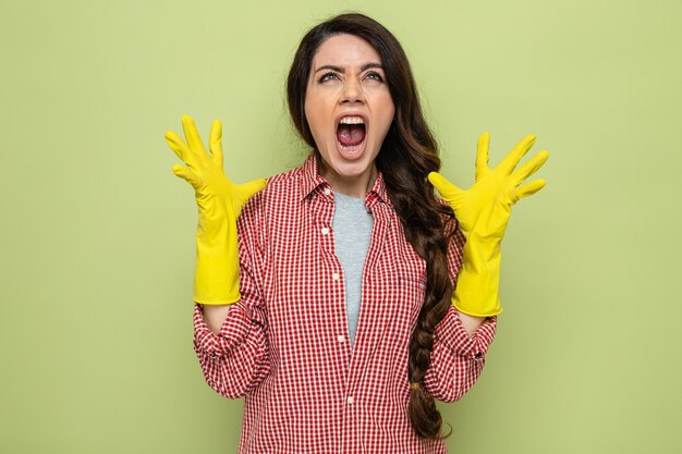 Mujer limpiadora bastante caucásica molesta con guantes de goma manteniendo las manos abiertas y mirando hacia arriba