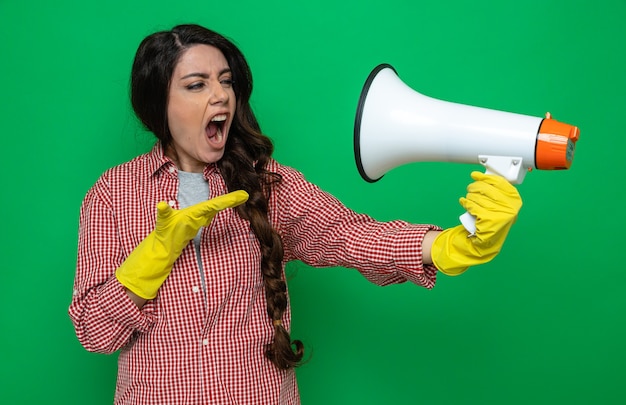 Mujer limpiadora bastante caucásica molesta con guantes de goma sosteniendo y mirando al altavoz manteniendo la mano abierta