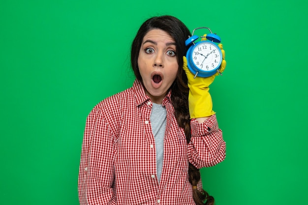 Foto gratuita mujer limpiadora bastante caucásica sorprendida con guantes de goma con reloj despertador