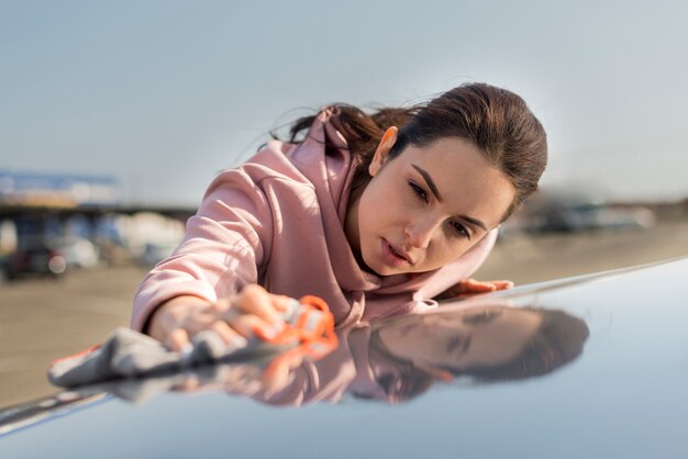 Mujer limpiando el capó de la vista frontal del coche