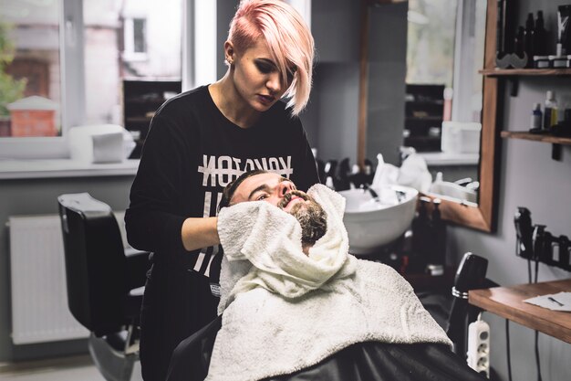 Mujer limpiando la cara del cliente en la barbería