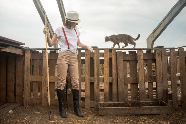 Mujer limpiando un gallinero con un gato