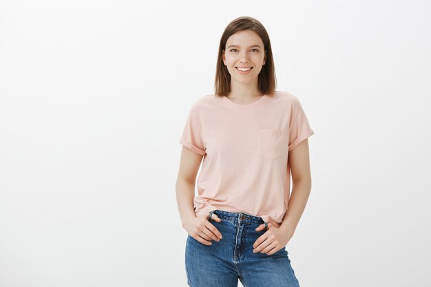 Mujer linda alegre que sonríe sobre la pared blanca con emoción feliz