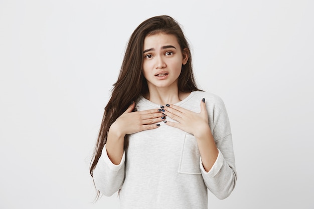 Mujer linda asombrada emocionada con el pelo largo y liso oscuro poniendo las manos en el pecho. Emociones, sentimientos, concepto de expresión facial