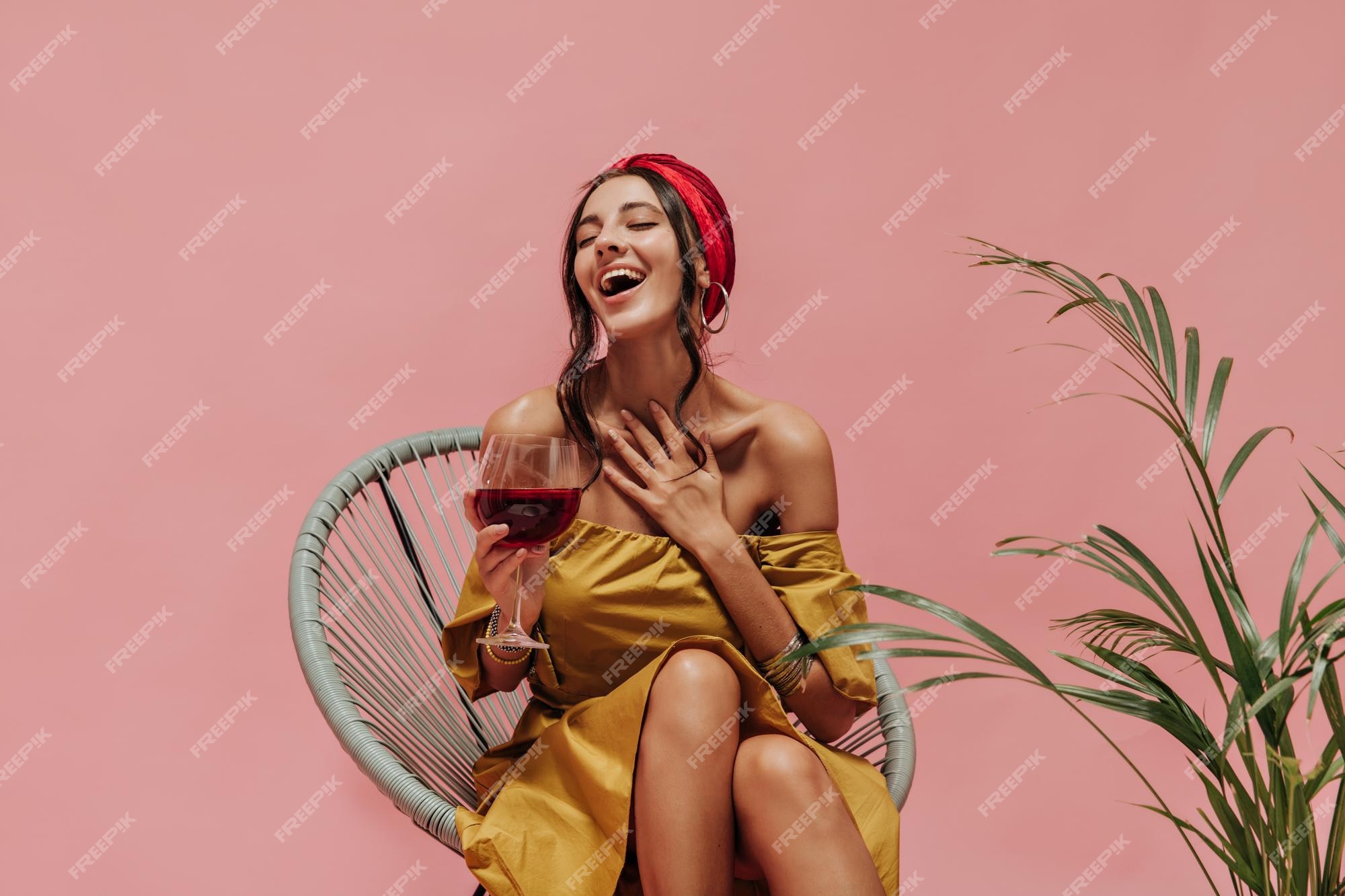 Mujer linda feliz con aretes de diadema roja y traje brillante de moda  riendo con los ojos cerrados y posando con vino