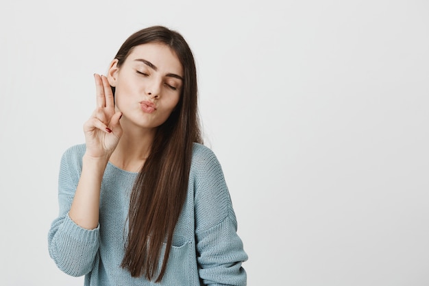 Mujer linda tonta muestra el signo de la paz y beso que sopla