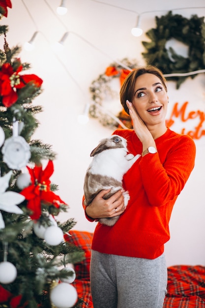 Mujer con lindo conejito por arbol de navidad