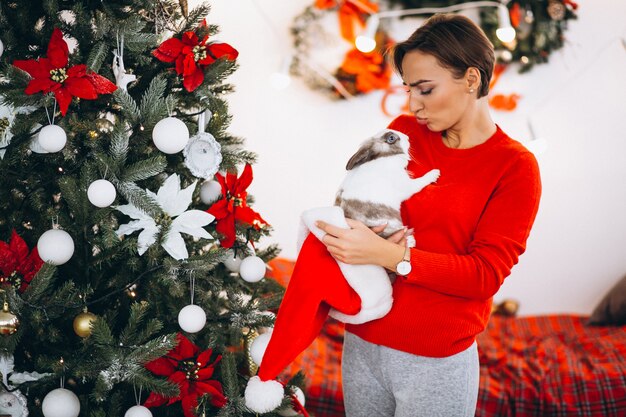 Mujer con lindo conejito por arbol de navidad