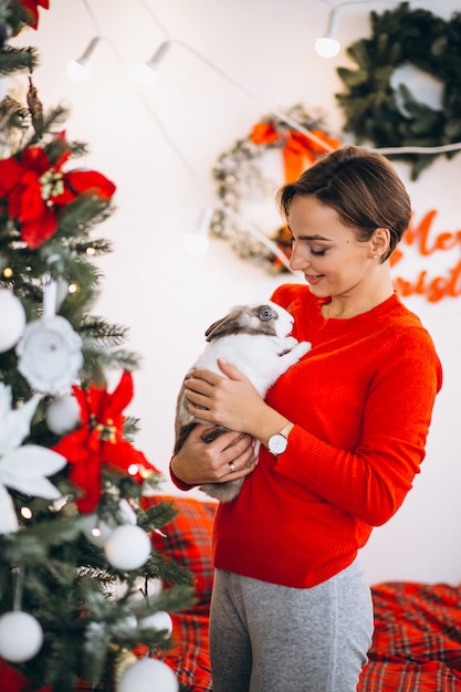 Mujer con lindo conejito por arbol de navidad