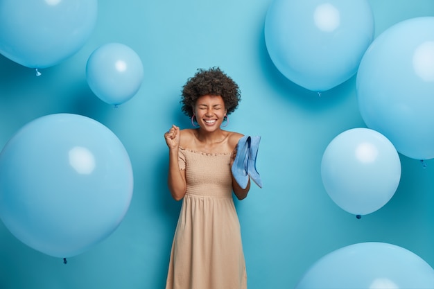 Mujer llena de alegría contenta de recibir los zapatos de su sueño como regalo de su novio, usa un vestido de cóctel largo de color beige, aprieta el puño con alegría, elige el mejor atuendo para la fiesta de graduación. mujeres, ropa, celebración