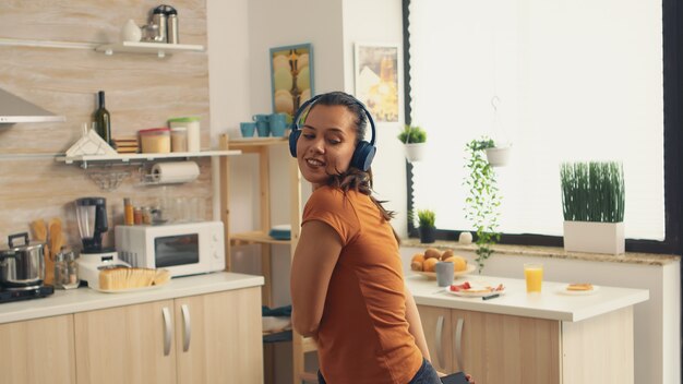 Mujer llena de felicidad bailando en la cocina durante el desayuno. Ama de casa enérgica, positiva, alegre, divertida y linda bailando sola en la casa. Entretenimiento y ocio solo en casa.