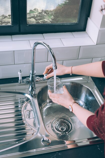 Mujer llenando el vaso con agua del grifo de acero en la cocina