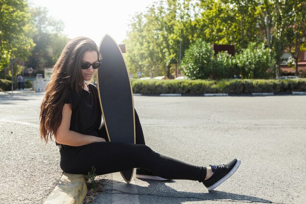 Mujer con longboard sentado en el pavimento