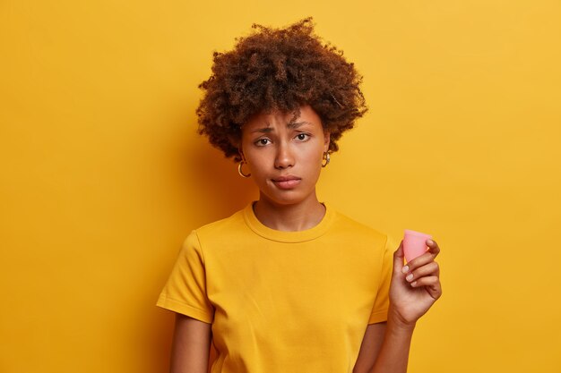 Mujer lúgubre disgustada que va a usar la copa menstrual por primera vez, piensa que son menos cómodos y efectivos que los tampones, inserta productos de higiene en la vagina para que no goteen ni manchen.