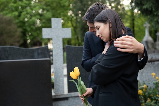 Mujer de luto en el cementerio siendo consolada por un hombre