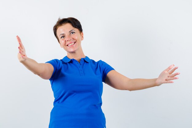 Mujer madura abriendo los brazos para abrazar en camiseta azul y mirando feliz. vista frontal.