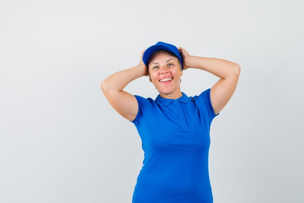 Mujer madura agarrando la cabeza entre las manos en camiseta azul y mirando contento.