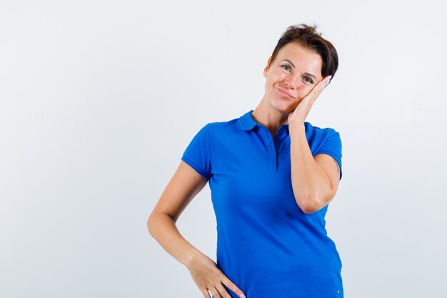 Mujer madura apoyándose en la palma de la mejilla en camiseta azul y mirando pensativo, vista frontal.