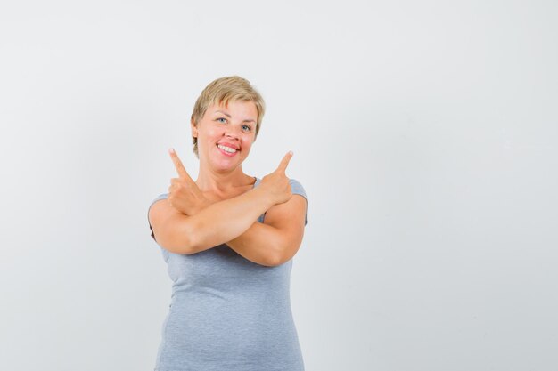 Mujer madura apuntando hacia arriba en camiseta gris y mirando alegre.