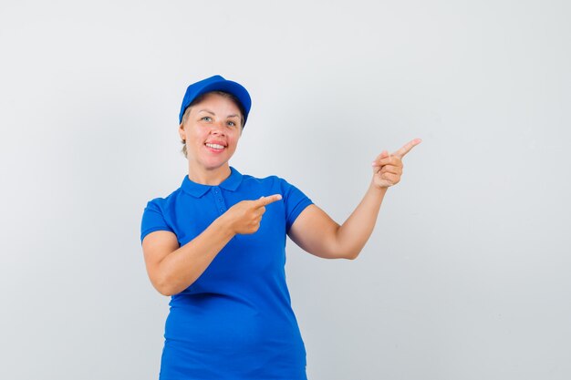 Mujer madura apuntando a la esquina superior derecha en camiseta azul y mirando alegre