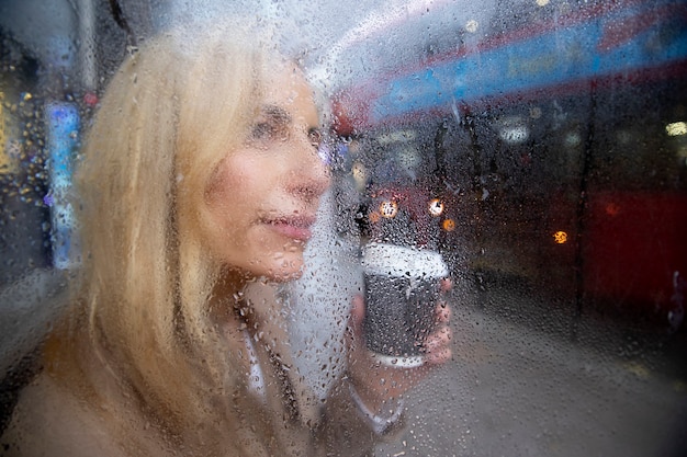 Mujer madura bebiendo un café afuera mientras llueve