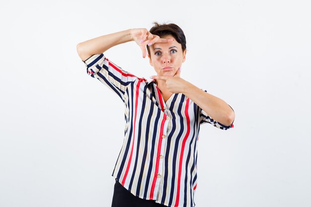 Mujer madura en blusa de rayas mostrando gesto de marco, labios curvados y mirada seria, vista frontal.