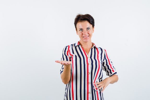 Foto gratuita mujer madura en camisa a rayas estirando la mano y mirando alegre, vista frontal.