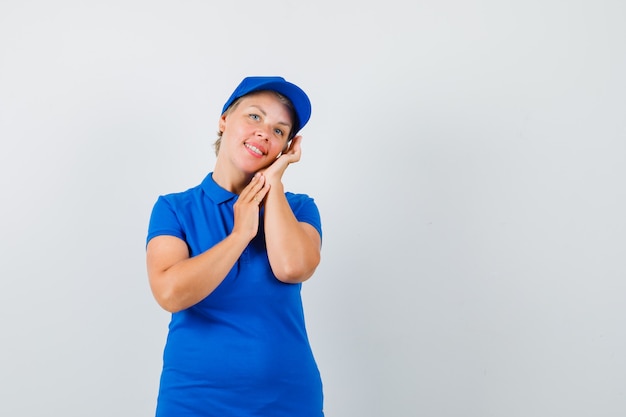Mujer madura en camiseta azul apoyándose en la mejilla de la palma y luciendo bonita.