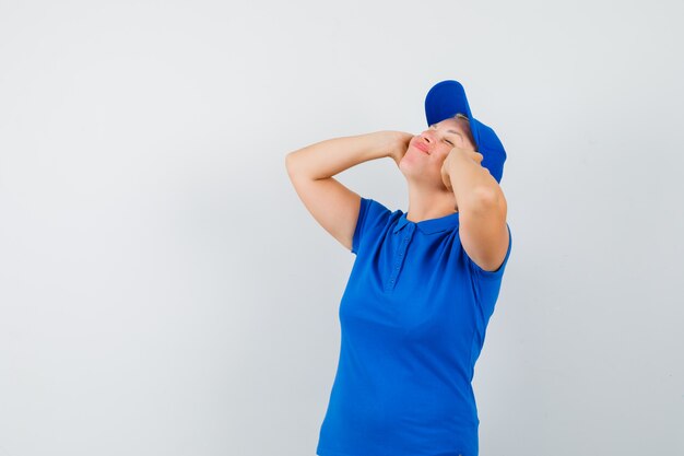 Mujer madura en camiseta azul cogidos de la mano en los oídos y buscando pacífica.