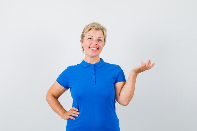 Mujer madura en camiseta azul fingiendo sostener o mostrar algo y mirando alegre.