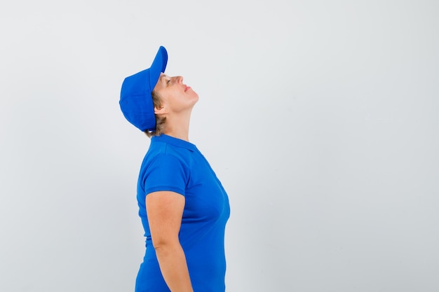 Mujer madura en camiseta azul inclinando la cabeza hacia atrás y mirando pacífica.