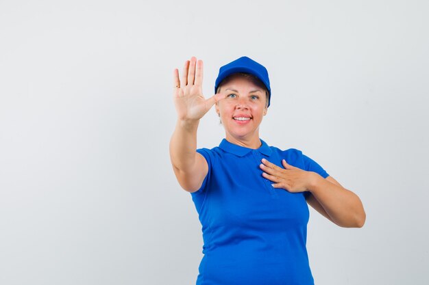 Mujer madura en camiseta azul mostrando gesto de parada y mirando confiado