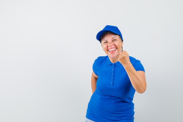 Mujer madura en camiseta mostrando el puño cerrado y mirando feliz