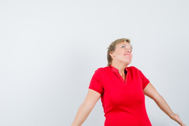 Mujer madura en camiseta roja encogiéndose de hombros y mirando confundido