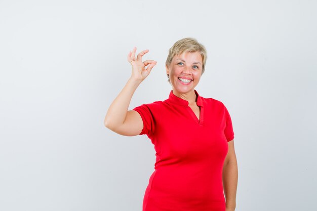 Mujer madura en camiseta roja mostrando gesto ok y mirando alegre