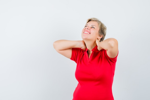 Mujer madura en camiseta roja que sufre de dolor de cuello y parece fatigado