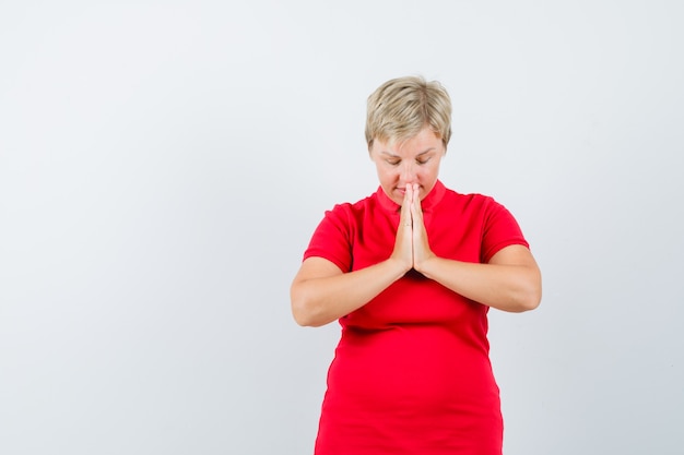 Mujer madura cogidos de la mano en gesto de oración en camiseta roja y mirando esperanzado