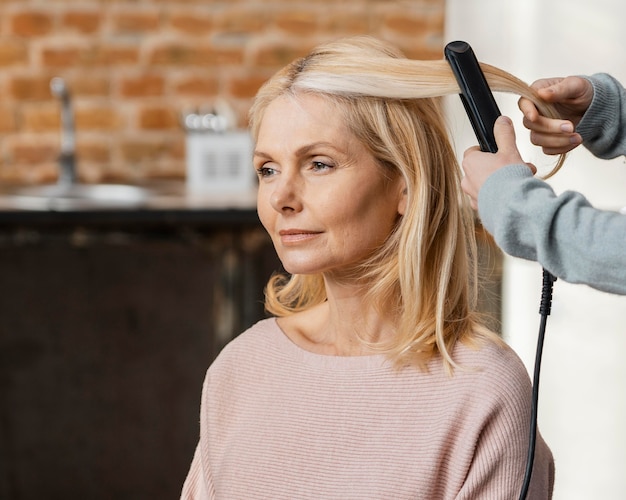 Mujer madura consiguiendo su cabello alisado por peluquero en casa