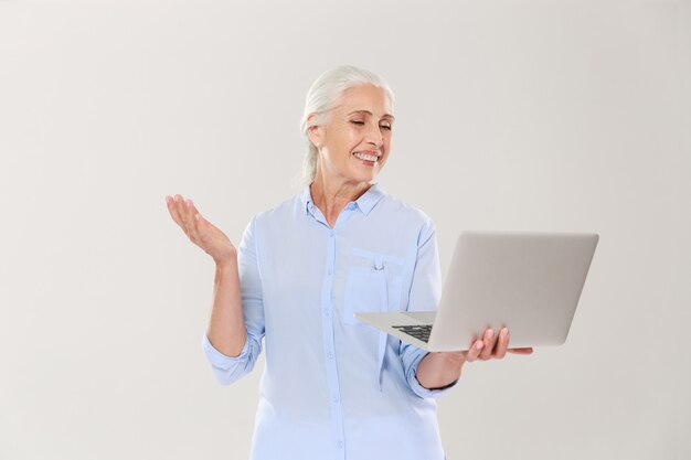 Mujer madura divertida que usa la computadora portátil aislada sobre blanco